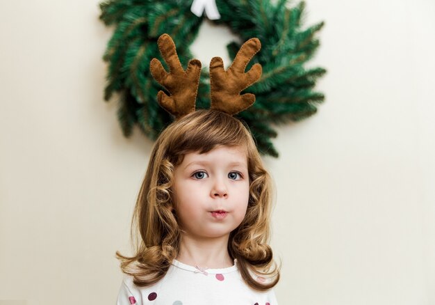 Petite fille drôle avec une couronne de Noël. Style minimaliste. Enfant mignon avec des cornes de cerf.