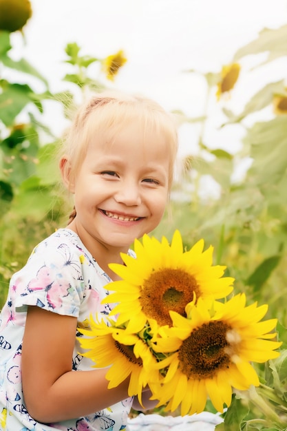 Petite fille drôle dans le domaine avec des fleurs de tournesol, heure d'été