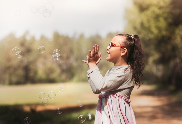 Petite fille drôle joue avec des bulles de savon dans la nature en été