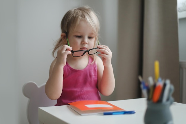 petite fille drôle à lunettes écrivant et dessinant à la table