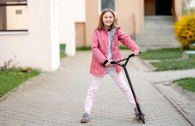 La petite fille drôle monte un scooter de coup-de-pied