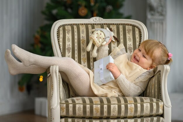 Petite fille drôle s'amusant sur une chaise devant l'arbre de Noël