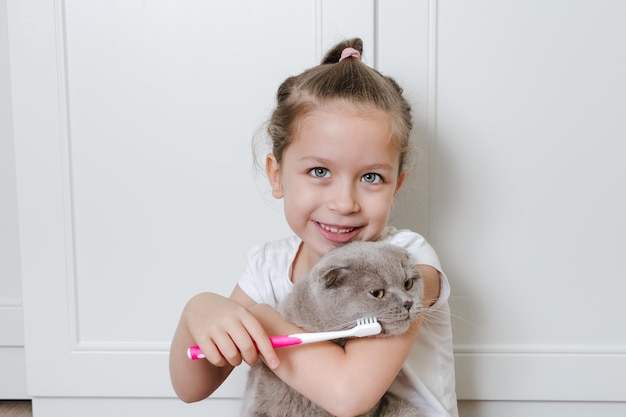 La petite fille drôle se brosser les dents du chat avec une brosse à dents Concept de santé pour animaux de compagnie