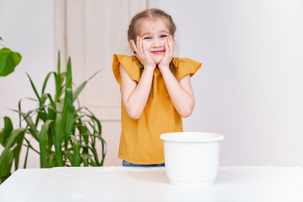 Petite fille drôle tient les mains dans la farine sur ses joues. passe-temps culinaire des enfants. Recette simple et délicieuse. École culinaire.