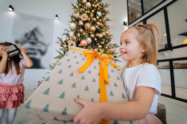 La petite fille avec du charme tient un cadeau sur un fond des arbres de Noël