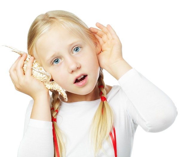 Petite fille écoutant un shell isolé sur fond blanc