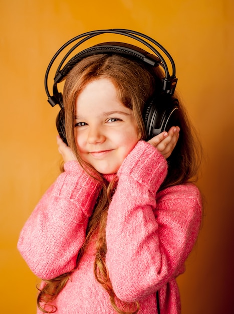 petite fille écoute de la musique sur un casque sur fond jaune