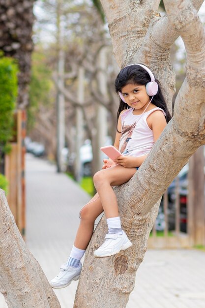 Petite fille écoute de la musique avec ses écouteurs sur un arbre