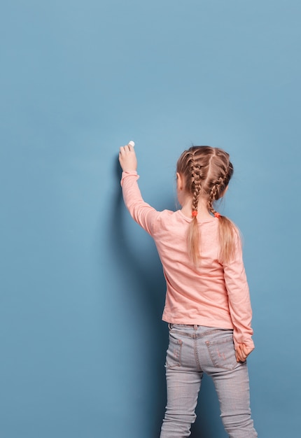 Petite fille écrit à la craie sur le mur bleu