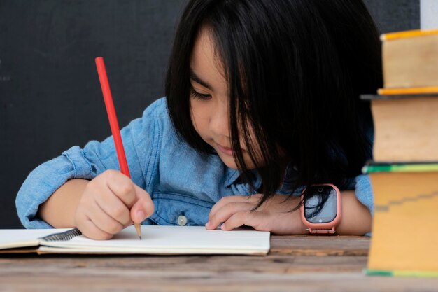 Petite fille écrivant quelque chose dans un cahier et assise à table étudiante étudiant à la maison