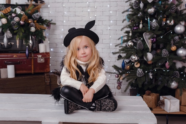 Petite fille élégante posant près de l'arbre du nouvel an en prévision de Noël.