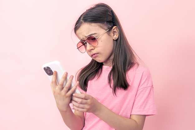 Petite fille élégante avec un smartphone sur fond rose