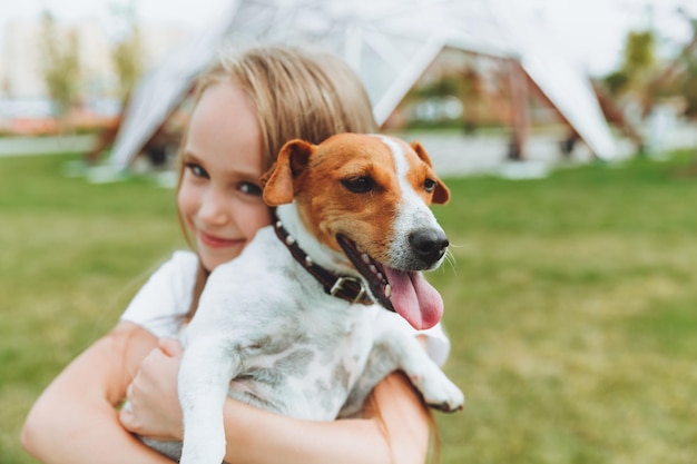 Une petite fille embrasse et étreint son chien terrier Jack Russell dans le parc L'amour entre le propriétaire et le chien un enfant tient un chien dans ses bras