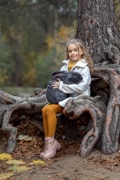 Une petite fille embrasse un lapin gris géant dans la forêt d'automne Concept amour de la nature et amour des animaux