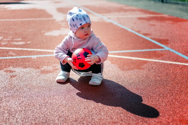 Petite fille enfant en bas âge avec boule rouge à l'aire de jeux