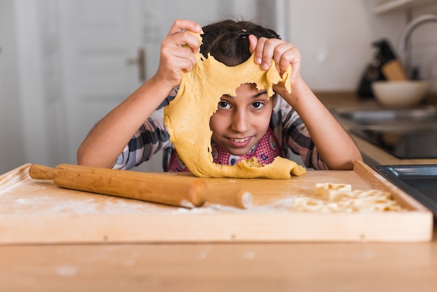 Petite fille enfant dans la cuisine habillée en tablier et écharpe comme chef. Fille rouler la pâte avec un rouleau à pâtisserie, sourit heureux. Concept de: nutrition, école de cuisine, éducation.