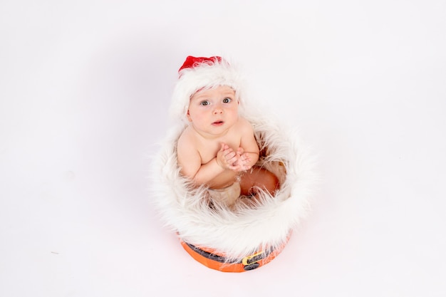 Une petite fille enfant est assise dans un bonnet de Noel sur un fond blanc isolé avec ses mains, demandant un cadeau, bonne année 2021, espace pour le texte.