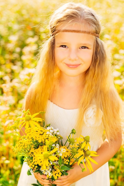 Petite fille enfant heureuse sur une prairie d'été dans la nature tient un bouquet de fleurs jaunes et sourit