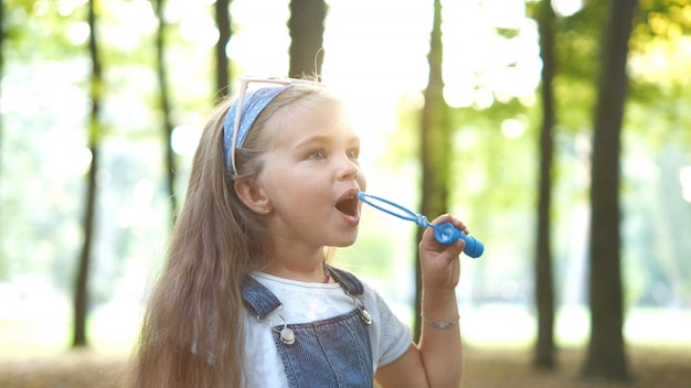 Petite fille enfant heureuse soufflant des bulles de savon à l'extérieur dans le parc d'été