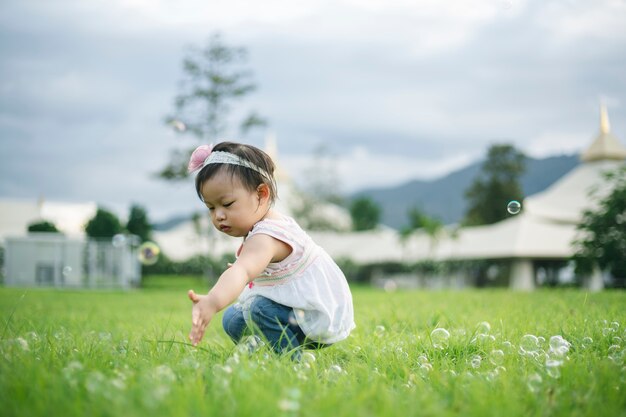 Petite fille enfant jouant avec des bulles sur l'herbe verte à l'extérieur dans le parc.