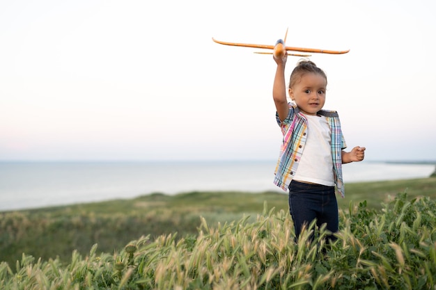 Petite fille enfant lance un avion jouet dans le ciel bébé se promène sur le terrain au coucher du soleil dans l'enfance d'été et le concept de mode de vie sain