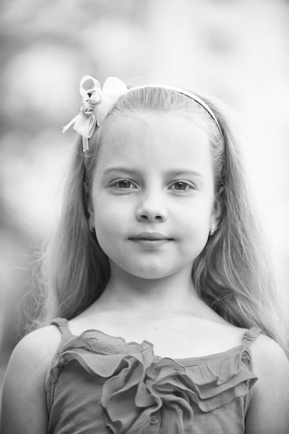 Petite fille ou enfant mignon avec un adorable visage souriant et un arc dans les cheveux blonds en gilet bleu en plein air sur fond flou