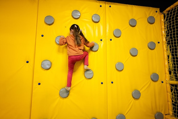 Petite fille enfant mur d'escalade au parc de jeux jaune Enfant en mouvement pendant les divertissements actifs