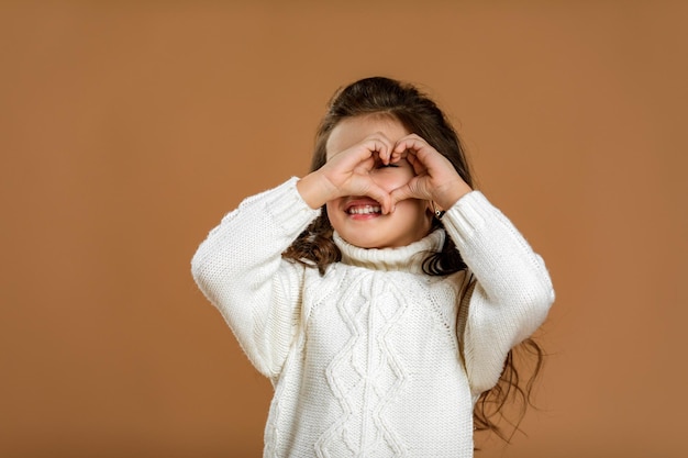 Petite fille enfant en pull blanc faisant un geste en forme de coeur