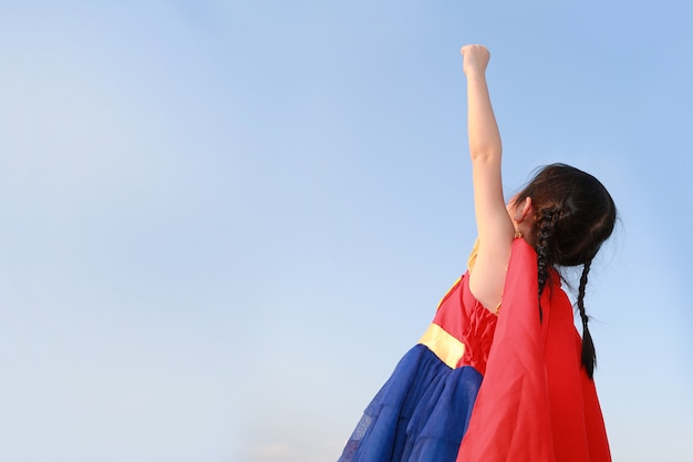 Petite fille enfant super-héros dans un geste pour voler sur fond de ciel bleu clair. Concept de super héros de gamin.