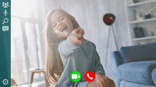 Petite fille enjouée souriante et jouant avec une baguette magique tout en ayant un appel vidéo