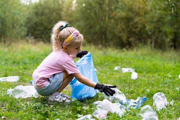 Une petite fille enlève les déchets plastiques et les met dans un sac poubelle biodégradable à l'extérieur. Le concept d'écologie, de traitement des déchets et de protection de la nature. Protection environnementale.