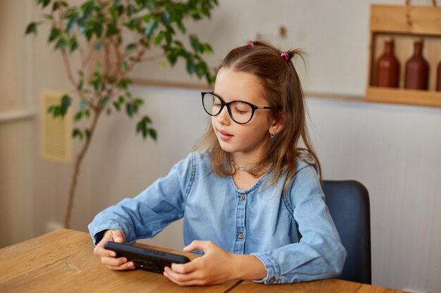 La petite fille enlève les lunettes en se frottant les yeux fatigués de jouer au jeu sur smarthone enfant mauvaise vue dépendance du gadget