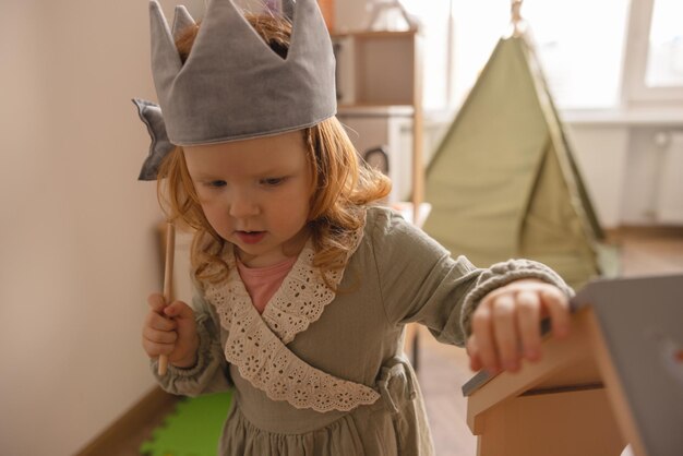 Petite fille enthousiaste à la peau claire avec des cheveux rouges portant une robe avec des jouets dans sa chambre pendant la journée Concept de l'enfance