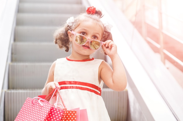 Petite fille sur l'escalator dans le centre commercial avec des achats