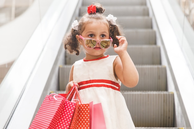 Petite fille sur l'escalator dans le centre commercial avec des sacs colorés