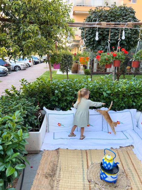 Petite fille essayant de caresser un chat roux sautant sur un tapis dans le jardin