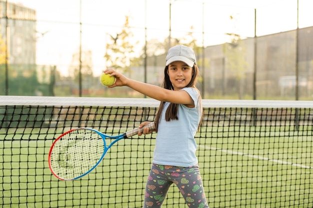 Petite fille essayant de jouer au tennis sur un court extérieur