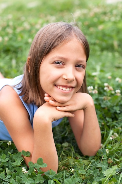 Une petite fille est allongée sur l'herbe dans le parc un jour d'été. il sourit et regarde la caméra. Enfance heureuse.