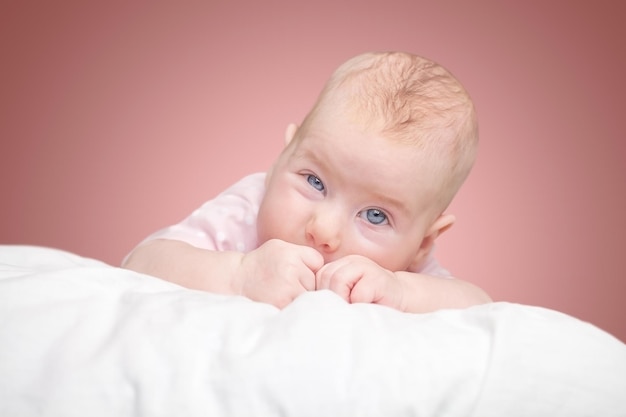 La petite fille est allongée sur un oreiller - nuage. sur fond rose.