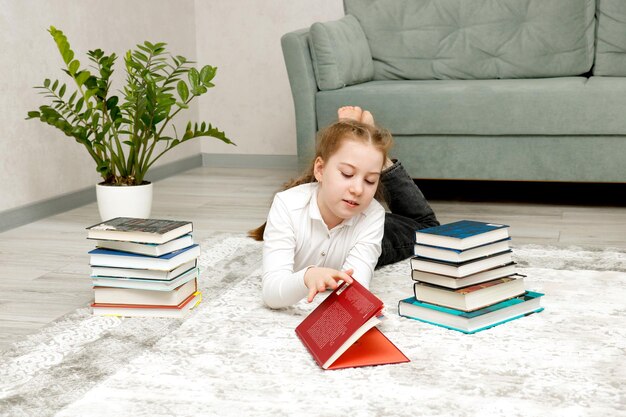 Une petite fille est allongée sur le sol à la maison entourée de livres.