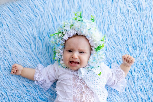 Une petite fille est allongée sur un tapis moelleux bleu dans un chapeau fait de fleurs et de pleurer