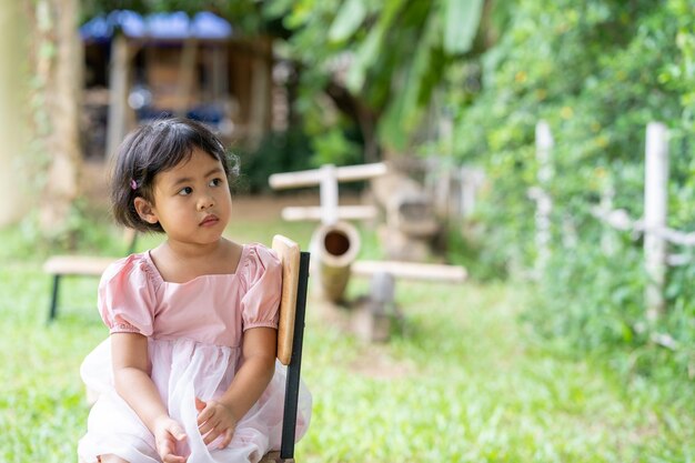 Une petite fille est assise sur une chaise dans un jardin en regardant le ciel.