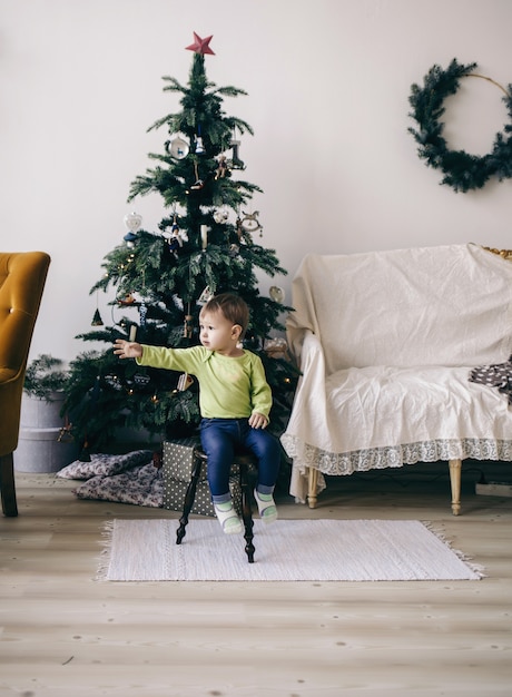 Une petite fille est assise sur une chaise en face de l'arbre de Noël