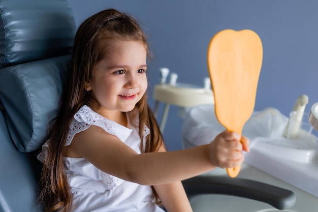 Une petite fille est assise sur une chaise et regarde son miroir.