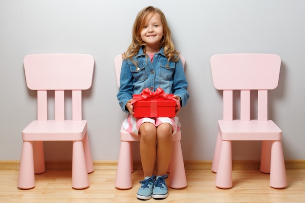 Petite fille est assise sur une chaise et tient une boîte avec un cadeau