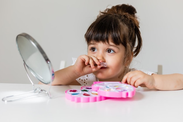 Petite fille est assise à la coiffeuse devant le miroir et se maquille comme maman