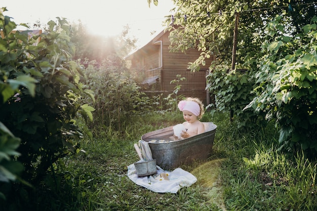 une petite fille est assise dans une baignoire en fer blanc avec des éclaboussures d'eau et se réjouit