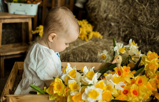 Une petite fille est assise dans une charrette en bois avec des fleurs jaunes et joue avec un canard jaune