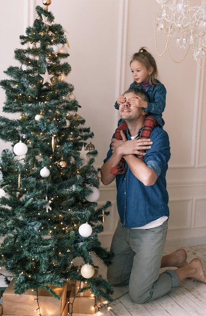 Une petite fille est assise sur les épaules de papa avec ses mains couvrant ses yeux arbre de Noël
