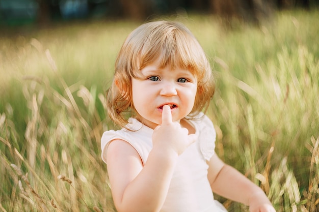 Petite fille est assise à l'extérieur et tient un doigt dans sa bouche.